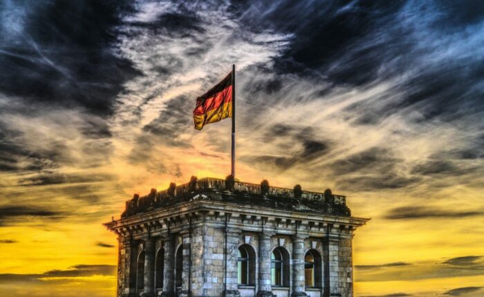 Gebäude mit der deutschen Flagge auf dem Dach vor einem dramatisch bewölkten Himmel bei Sonnenuntergang.