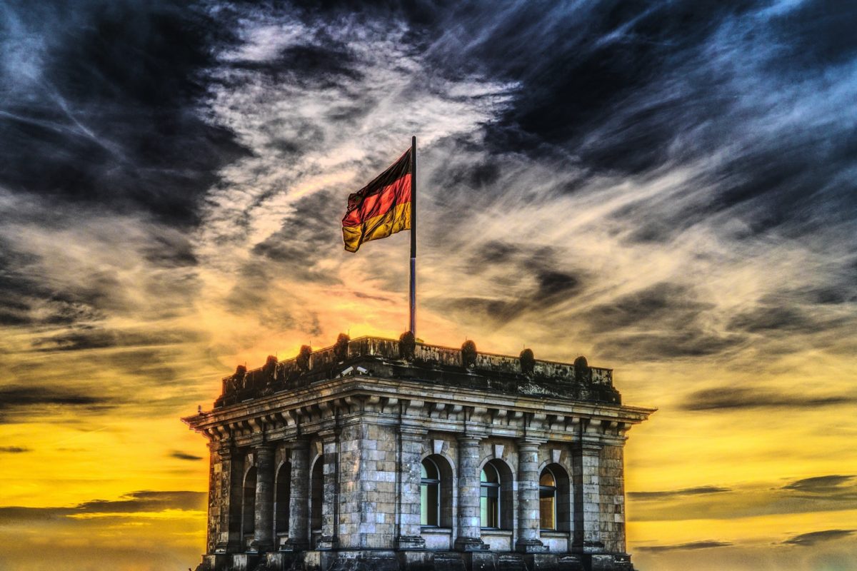 Gebäude mit der deutschen Flagge auf dem Dach vor einem dramatisch bewölkten Himmel bei Sonnenuntergang.