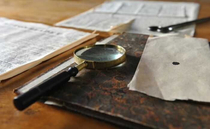 Lupe auf einem alten Schreibtisch mit historischen Dokumenten.