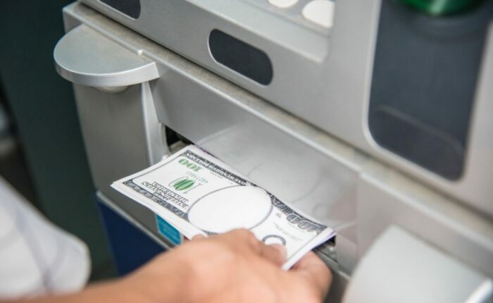 Person holt Geld aus einem Geldautomaten; sichtbar ist eine 100-Dollar-Note.