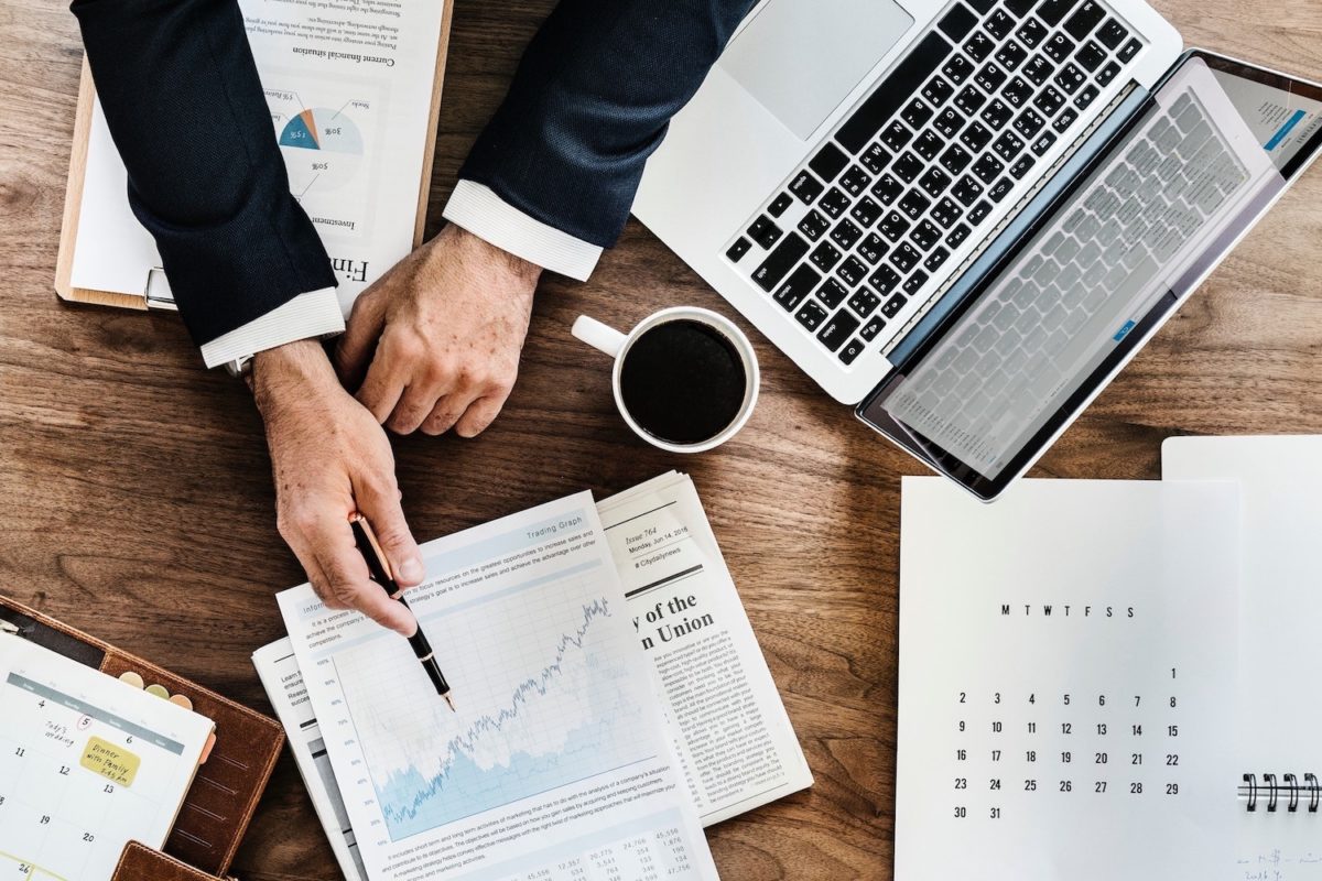 Mann analysiert Finanzdiagramme auf einem Papier, während er an einem Holztisch mit Laptop und Kaffee arbeitet.