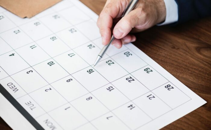 Männliche Hand markiert mit einem Stift Termine auf einem Papierkalender.