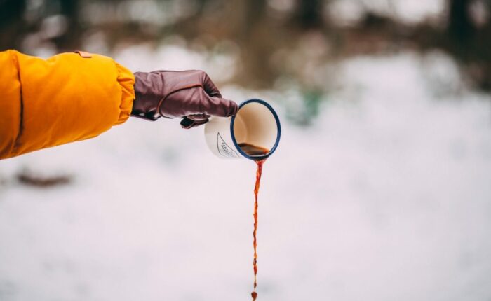 Person gießt Kaffee aus einem Emaille-Becher in den Schnee.