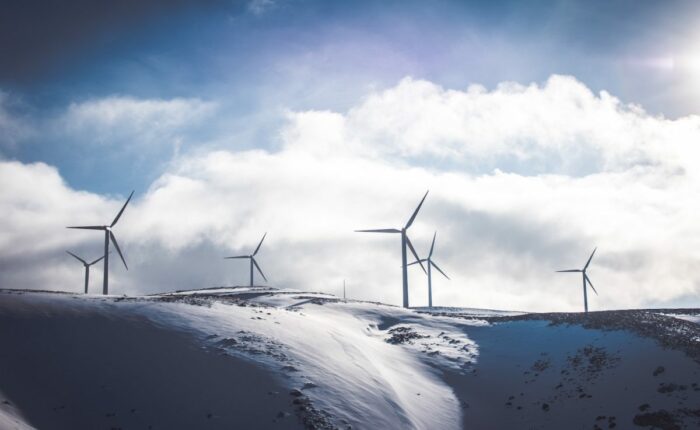 Windräder auf schneebedeckten Hügeln unter bewölktem Himmel.