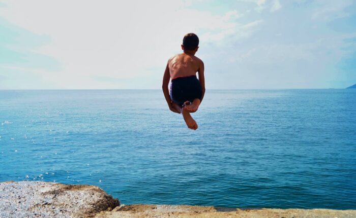 Kind springt von einer Klippe ins blaue Meer.