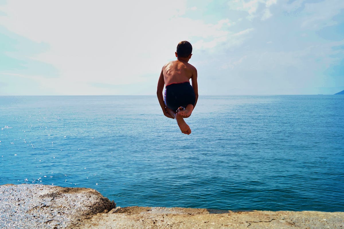 Kind springt von einer Klippe ins blaue Meer.